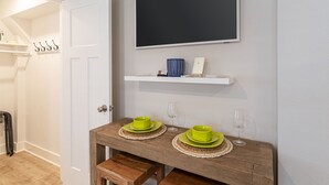 Ein Zimmer mit einem Holztisch, gedeckten grünen Tellern und Gläsern, einer weißen Tür und einem an der Wand befestigten Fernseher über einem Regal mit Dekorationen.