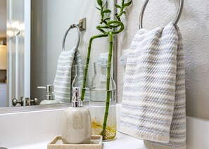 A bathroom with a mirror, a towel rack, a glass bottle, and a bamboo plant. - New, great for couples. Pets friendly, fenced backyard, close to beach and bay.  (KIll Devil Hills)