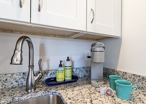 A kitchen with a stainless steel sink, a Keurig coffee maker, a dish soap dispenser, and two teal mugs on the counter. - New, great for couples. Pets friendly, fenced backyard, close to beach and bay.  (KIll Devil Hills)
