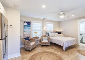A bedroom with a bed, two wicker chairs, a small table with a vase, a ceiling fan, and a painting on the wall. - New, great for couples. Pets friendly, fenced backyard, close to beach and bay.  (KIll Devil Hills)