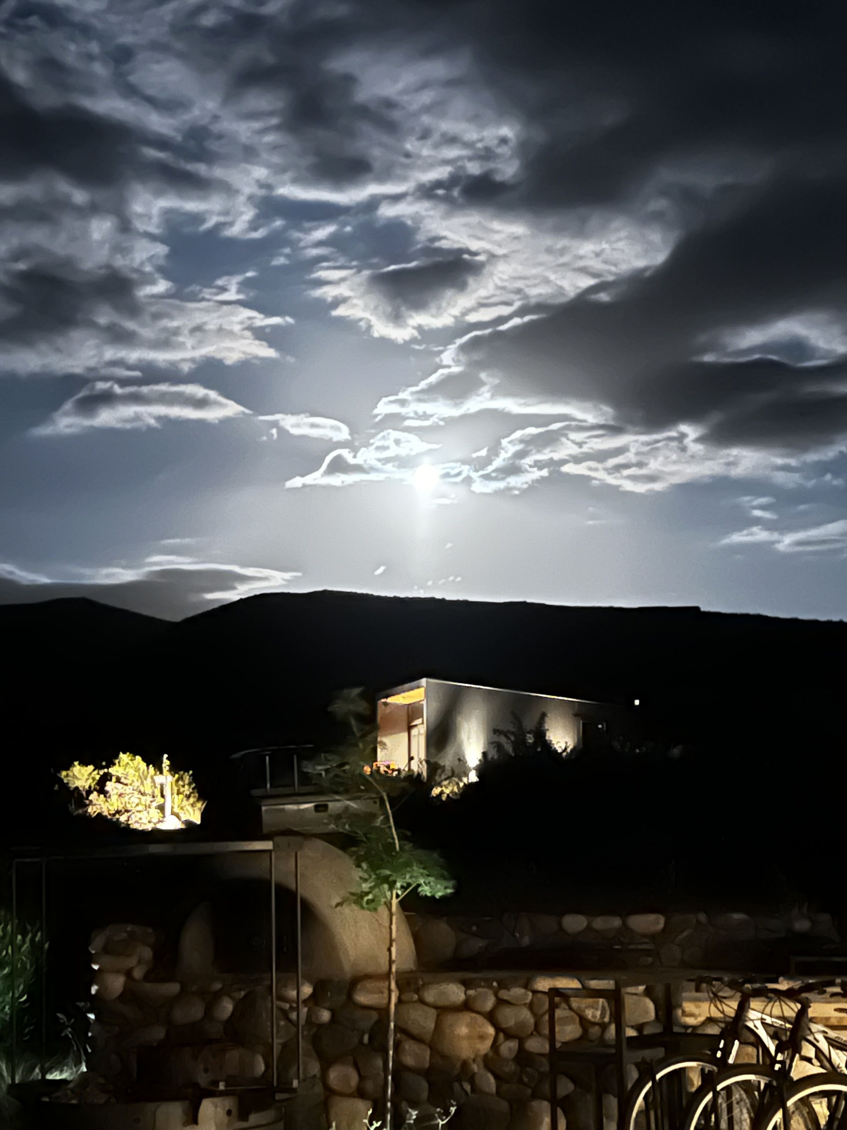 Vista noturna de uma casa com uma parede de pedra e uma bicicleta em primeiro plano.