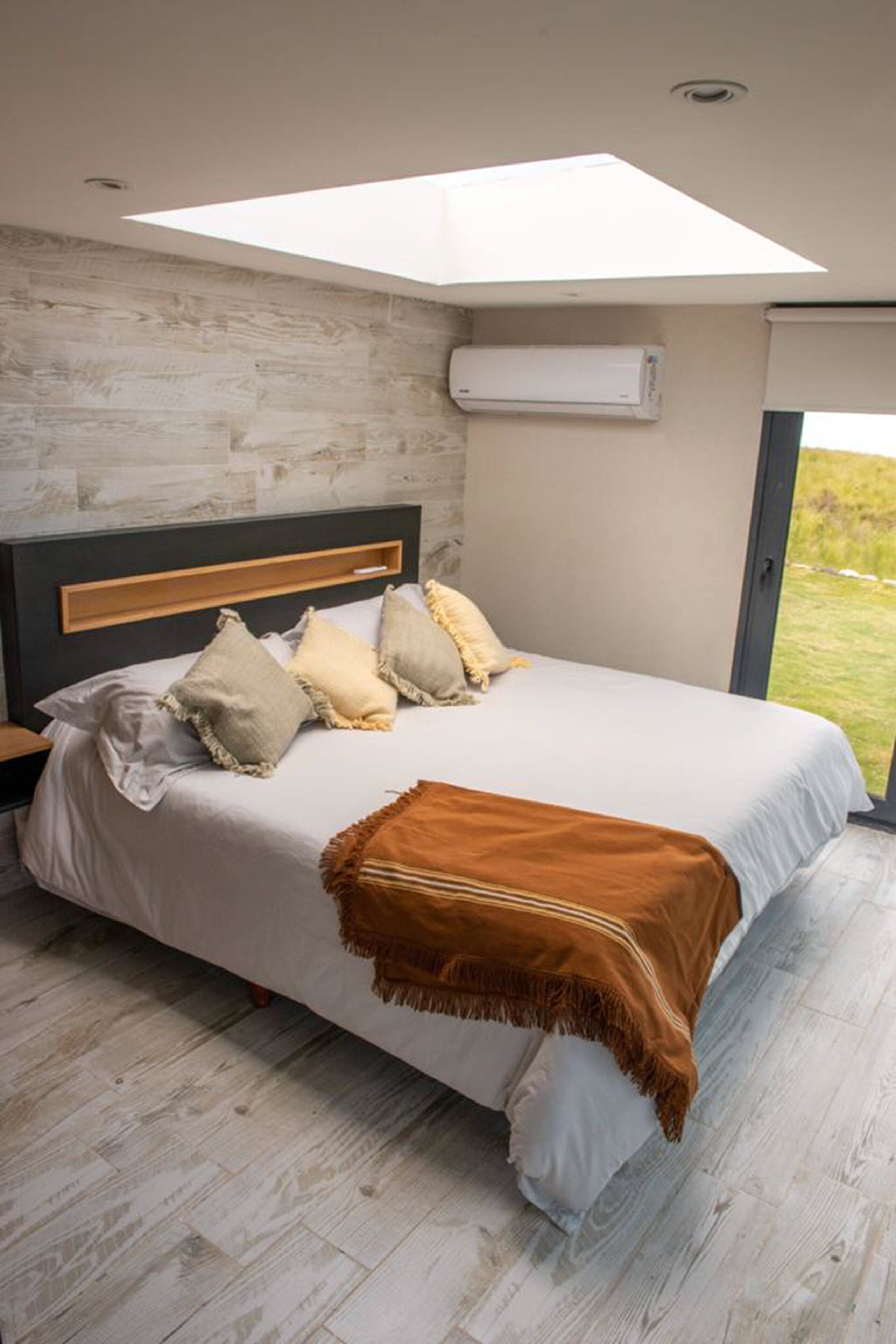 Camera da letto con un letto, cuscini, una coperta, un condizionatore d'aria a parete e un lucernario.