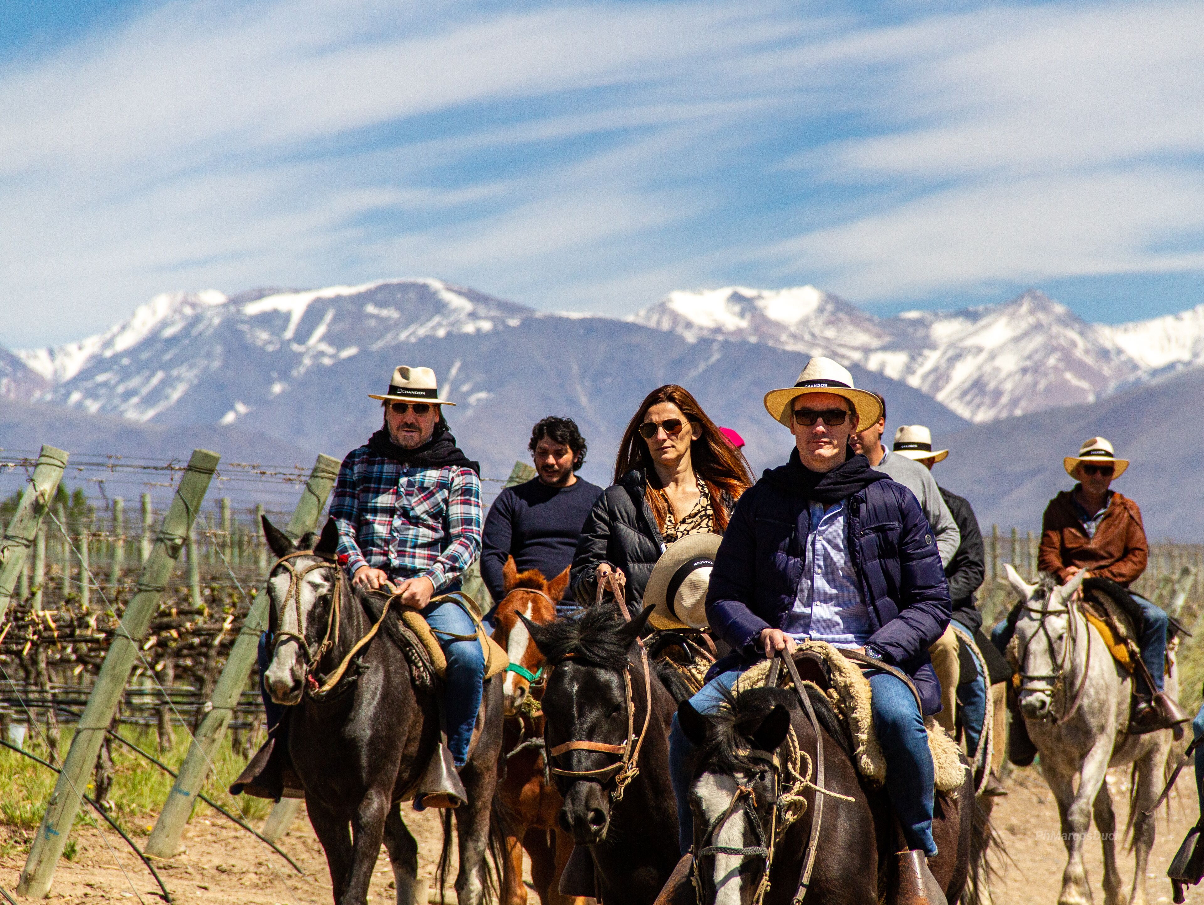 A group of people riding horses along a dirt path with a mountainous backdrop.