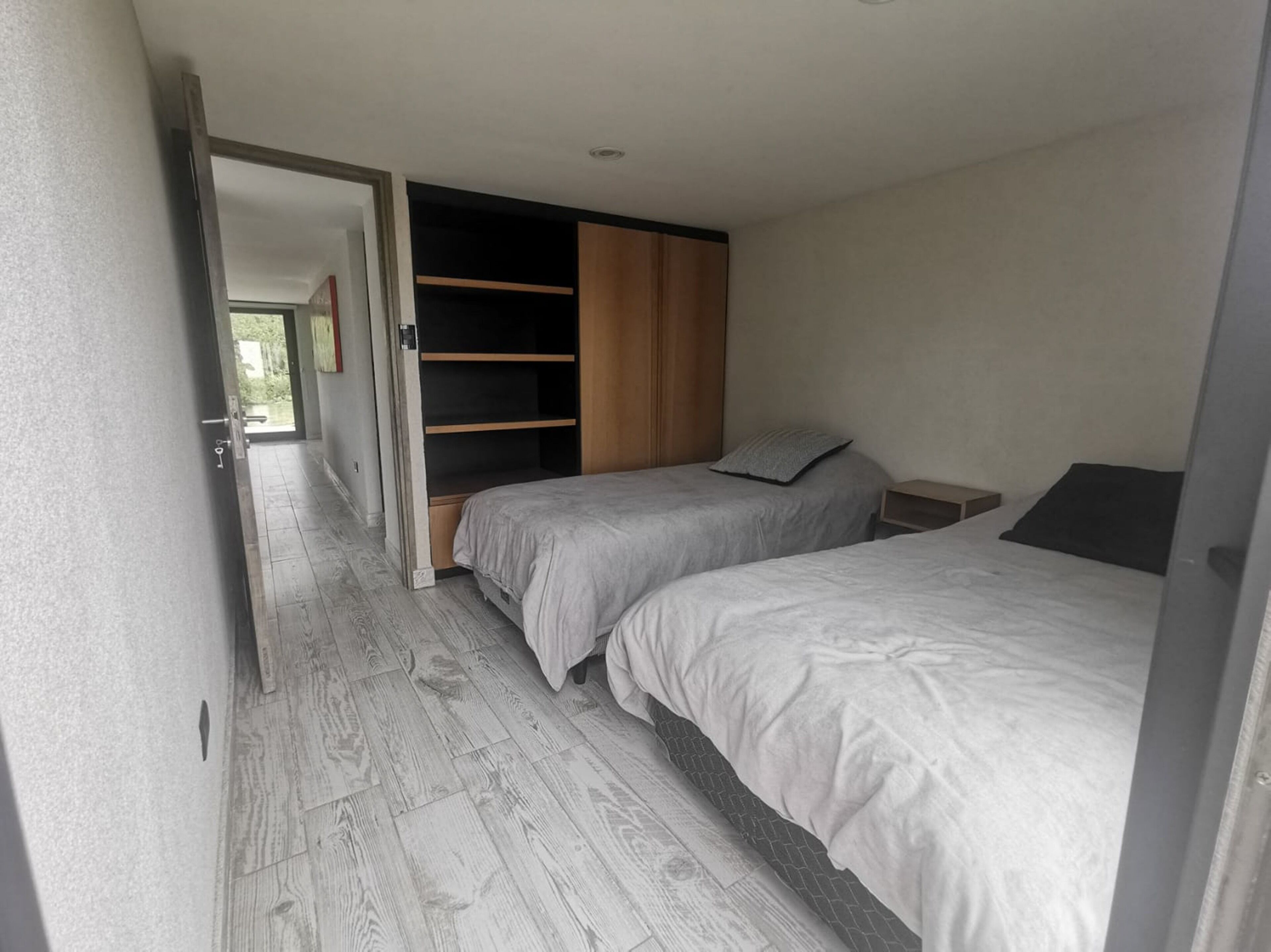 A bedroom with two beds, a wooden wardrobe, and a built-in shelving unit.