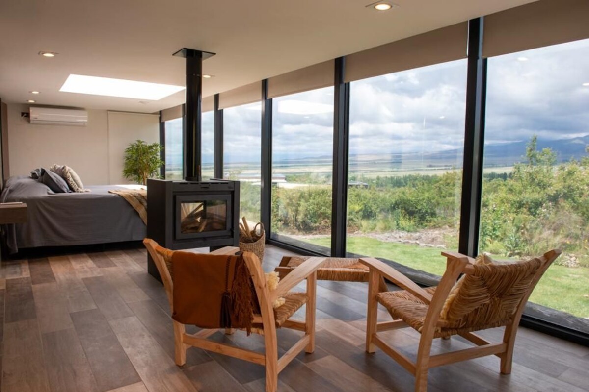 Un salon moderne doté d’une cheminée, de grandes fenêtres et offrant une vue sur l’extérieur.