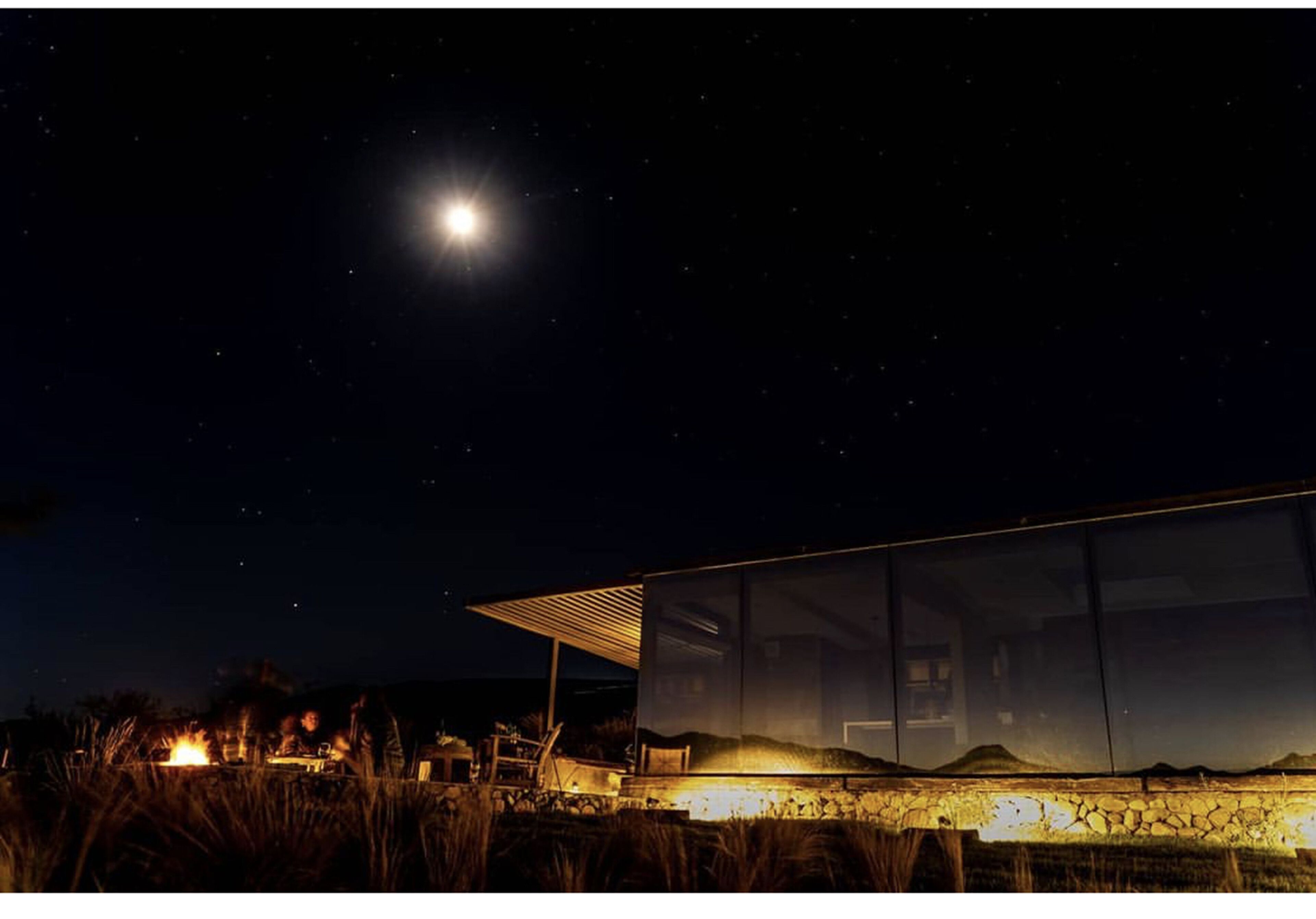 Una casa moderna con fachada de vidrio, una chimenea y un cielo nocturno despejado.