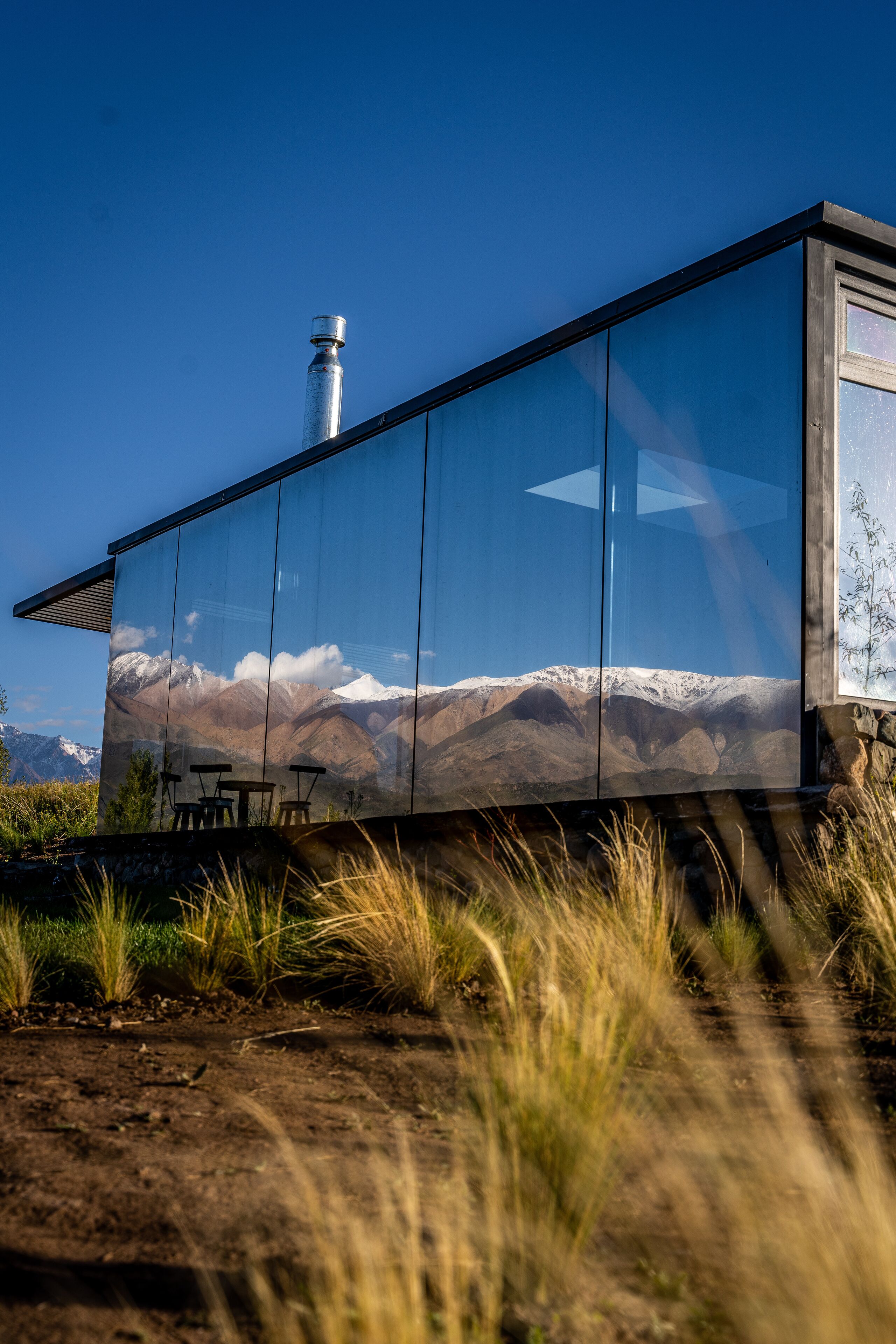 A modern building with a glass facade reflecting a mountainous landscape.