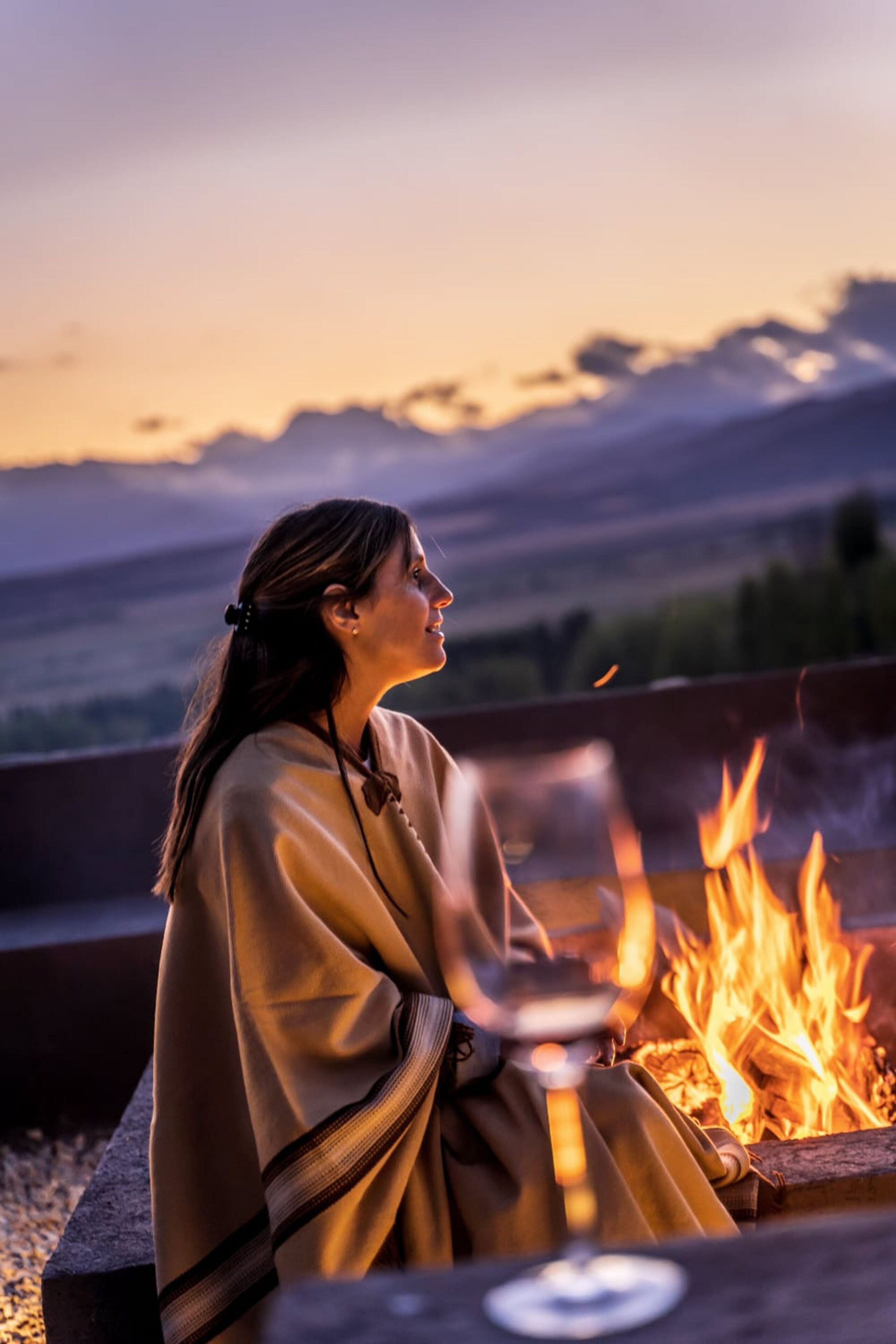 A person sitting by a campfire with a mountainous backdrop.
