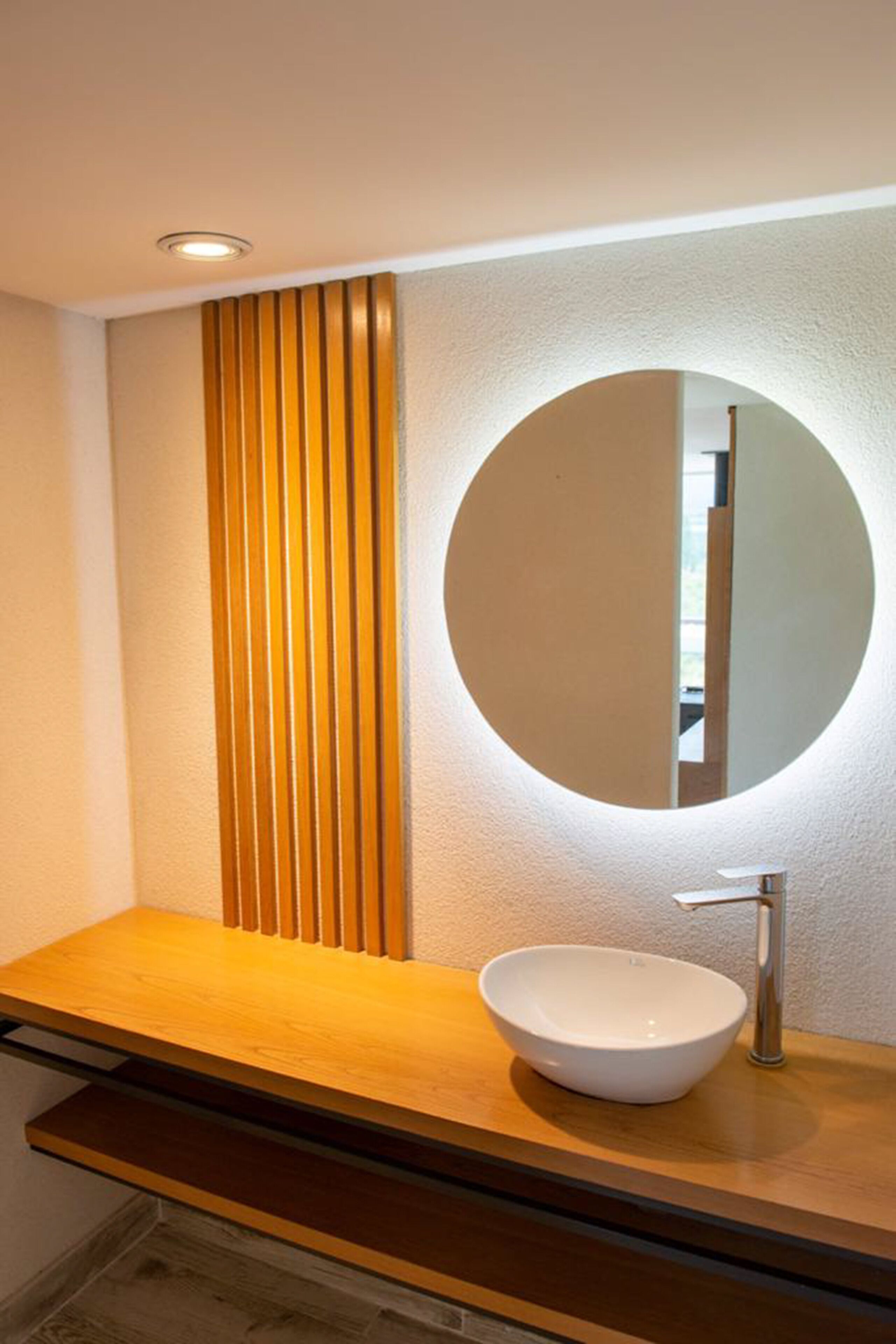 A modern bathroom with a wooden vanity, a round mirror, and a white sink.
