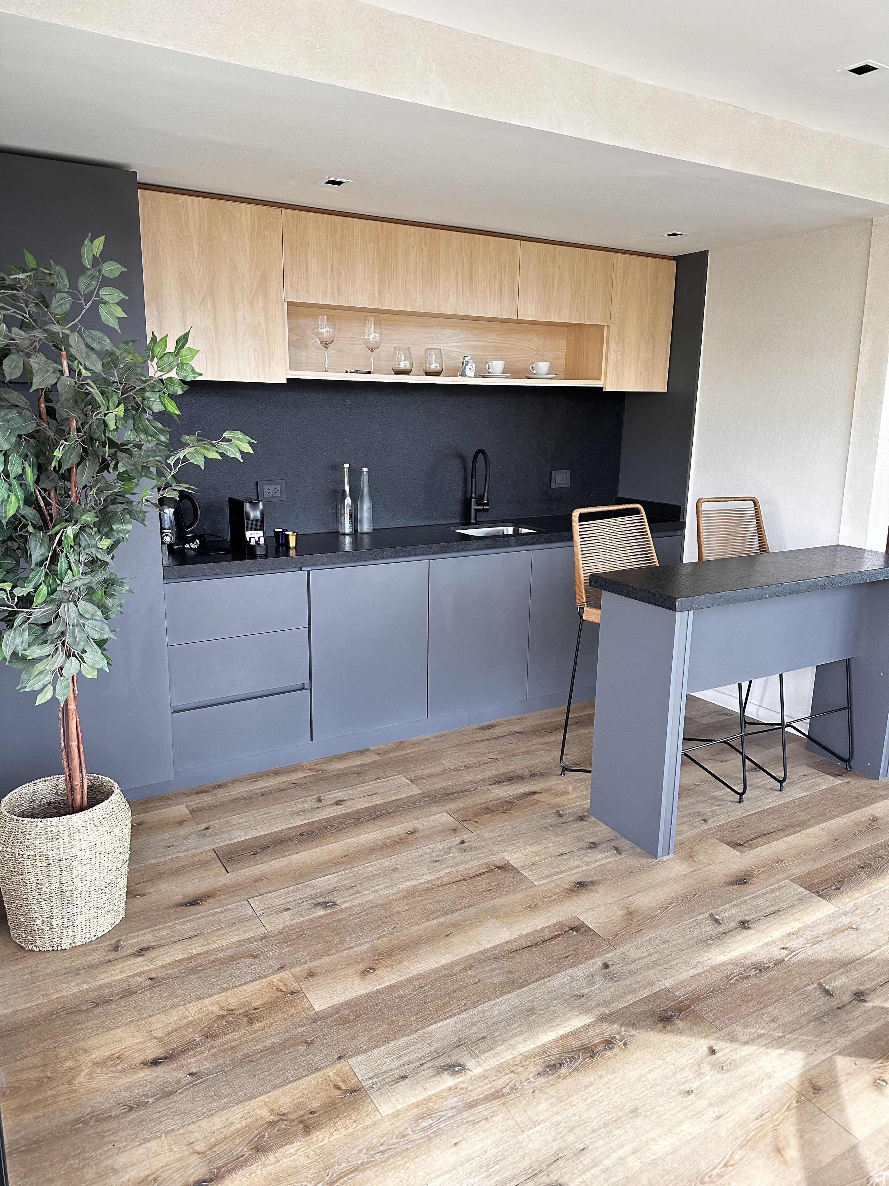A modern kitchen with grey cabinets, a black countertop, and a wooden dining table with chairs.