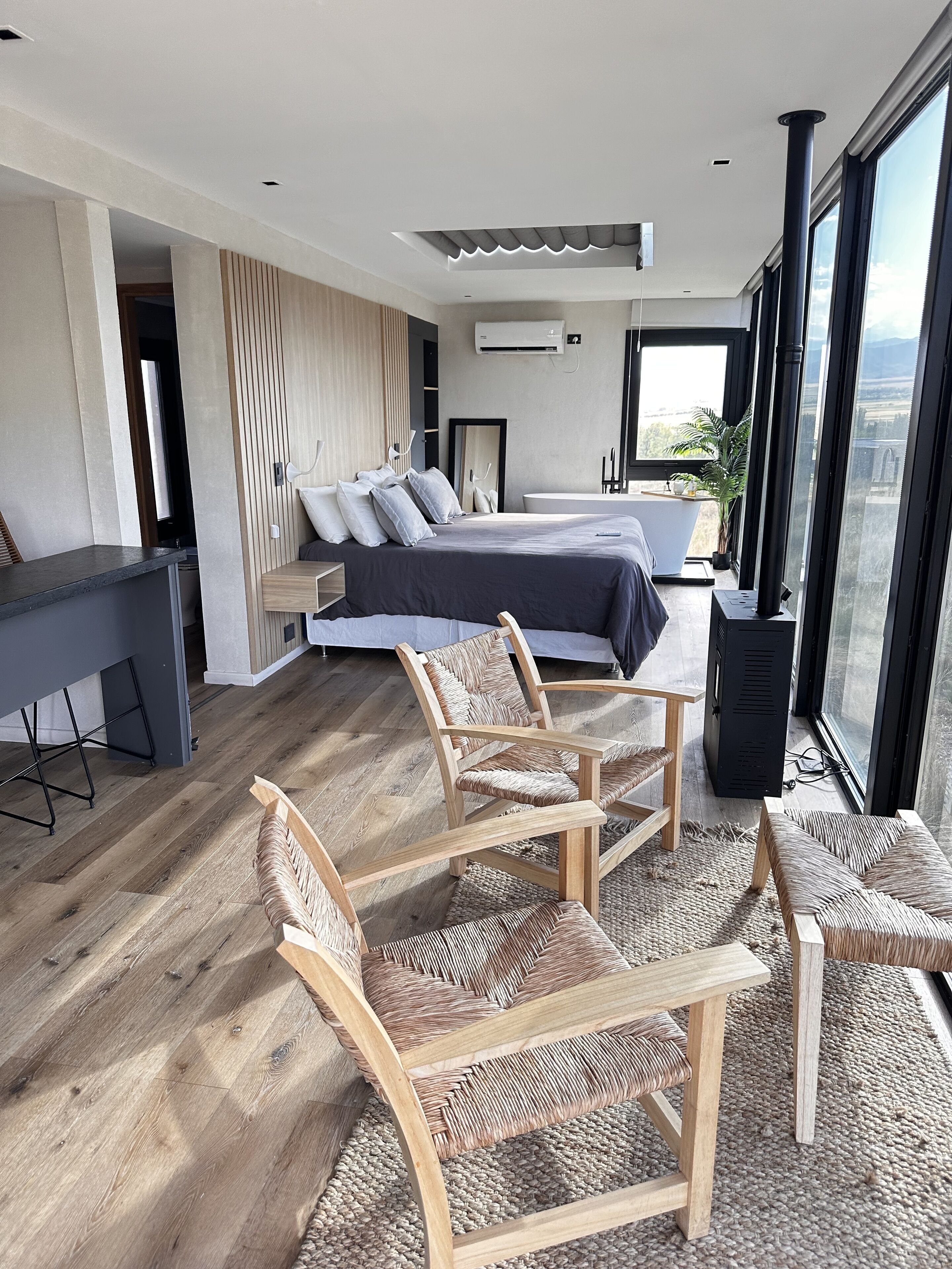 A modern bedroom with a large bed, a desk, and a view of the city through large windows.