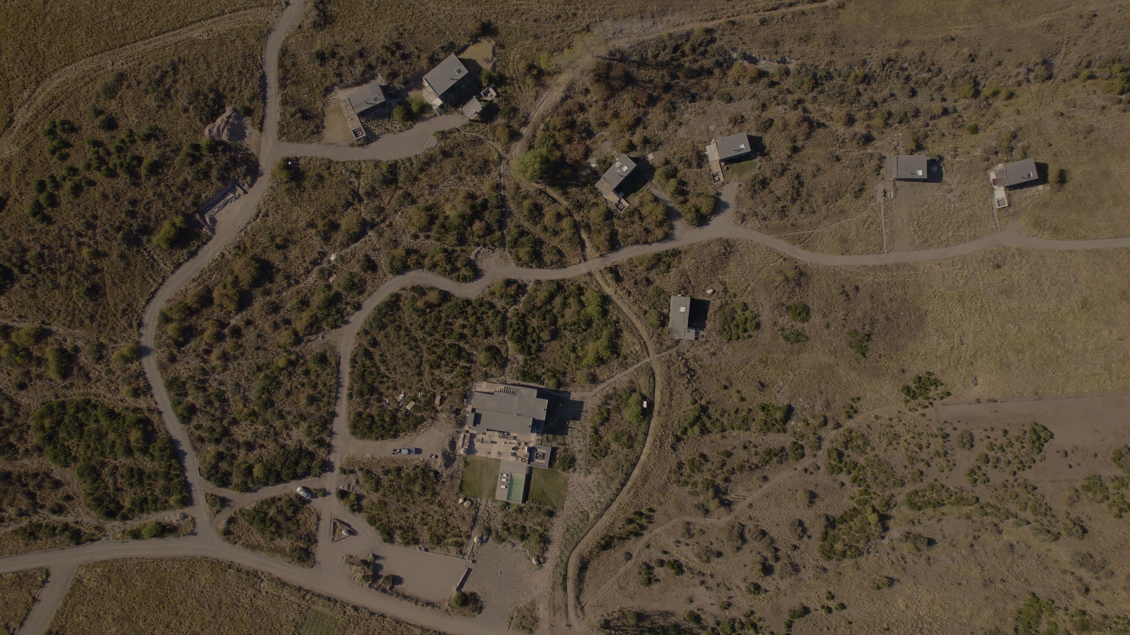 An aerial view of a rural area with several buildings, roads, and scattered vegetation.