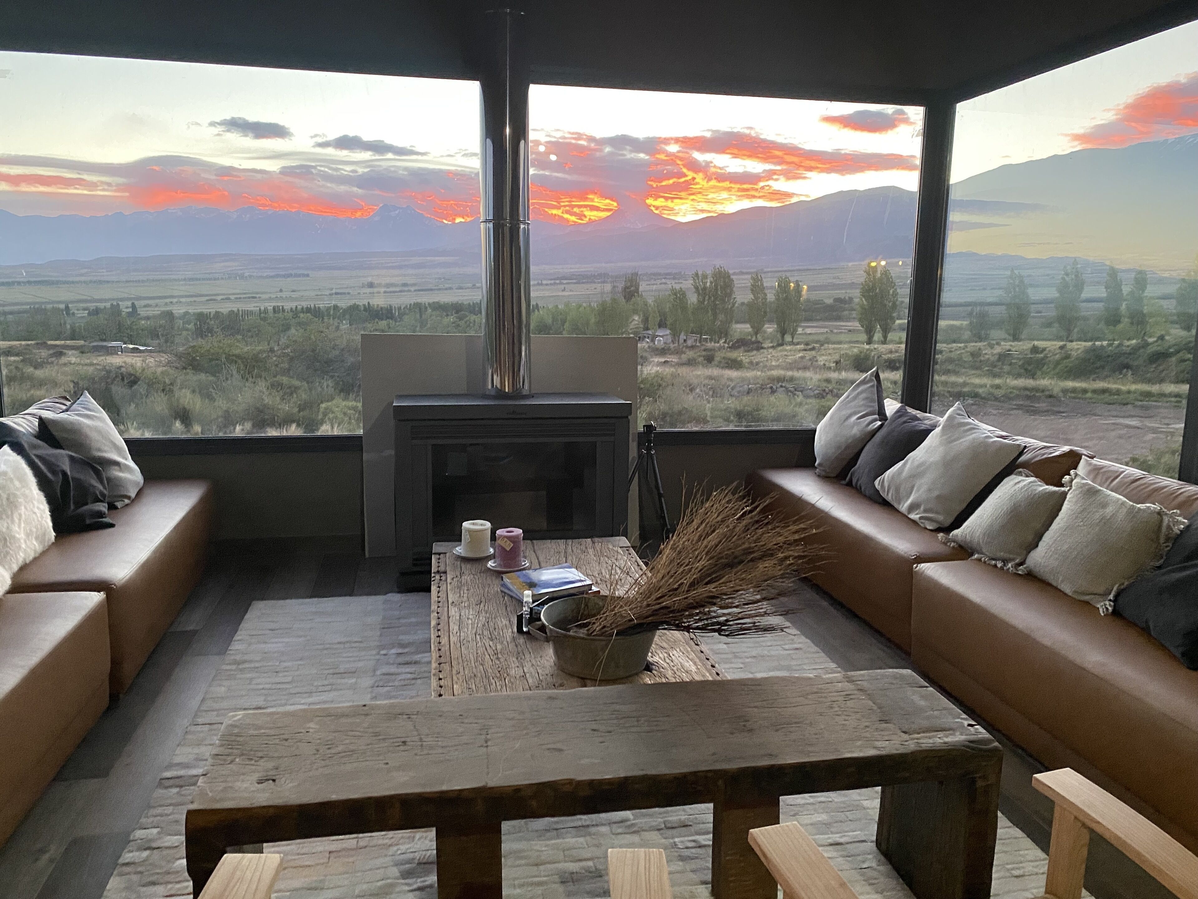A modern living room with a fireplace, a sofa, and a view of a sunset over a mountainous landscape.