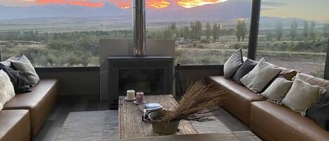 A modern living room with a fireplace, a sofa, and a view of a sunset over a mountainous landscape.