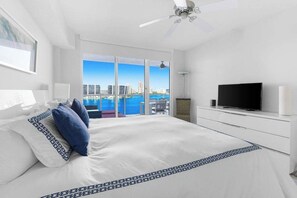 A hotel room with a large bed, a television, and a balcony with a view of the city.