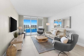 A modern living room with a sofa, armchair, coffee table, and a flat-screen TV.