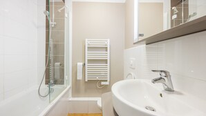 A modern bathroom with a glass-enclosed shower, a white sink, and a towel rack. - Némo - Appartement avec Terrasse (Courseulles-sur-Mer)