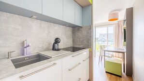 A modern kitchen with a built-in sink, a coffee machine, and a dining area with a table and chairs. - Némo - Appartement avec Terrasse (Courseulles-sur-Mer)