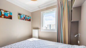 A bedroom with a bed, a window with curtains, and two paintings on the wall. - Némo - Appartement avec Terrasse (Courseulles-sur-Mer)