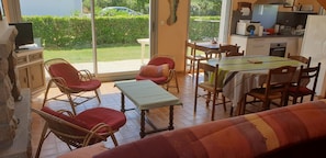 Un salón acogedor con muebles de mimbre, una mesa de comedor y una zona de cocina visible a través de una puerta corredera.