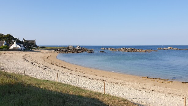 Una platja sorrenca amb mar blau clar, roques i un edifici blanc amb teulada verda.