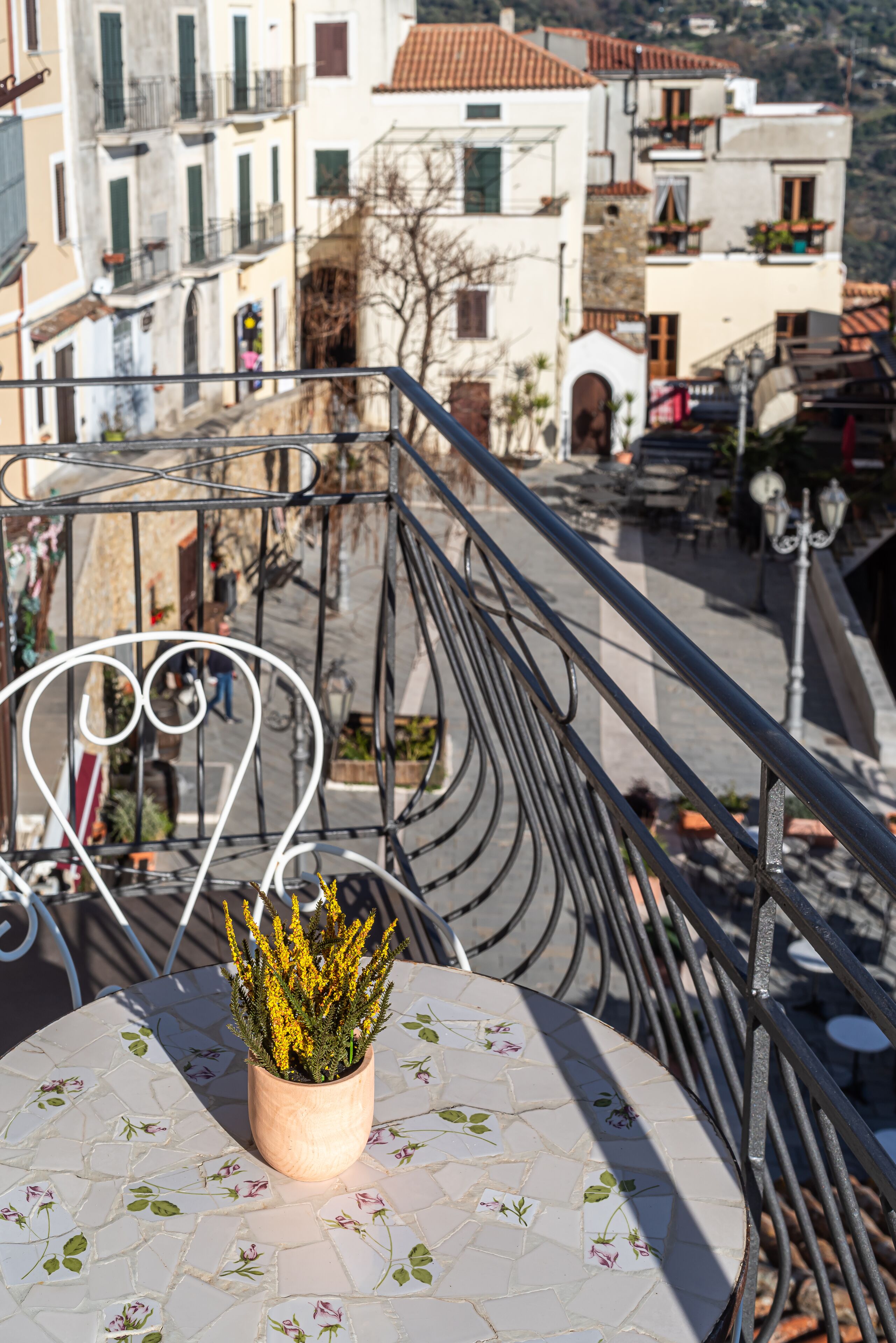 A balcony with a table and a potted plant, overlooking a street with buildings and a café.