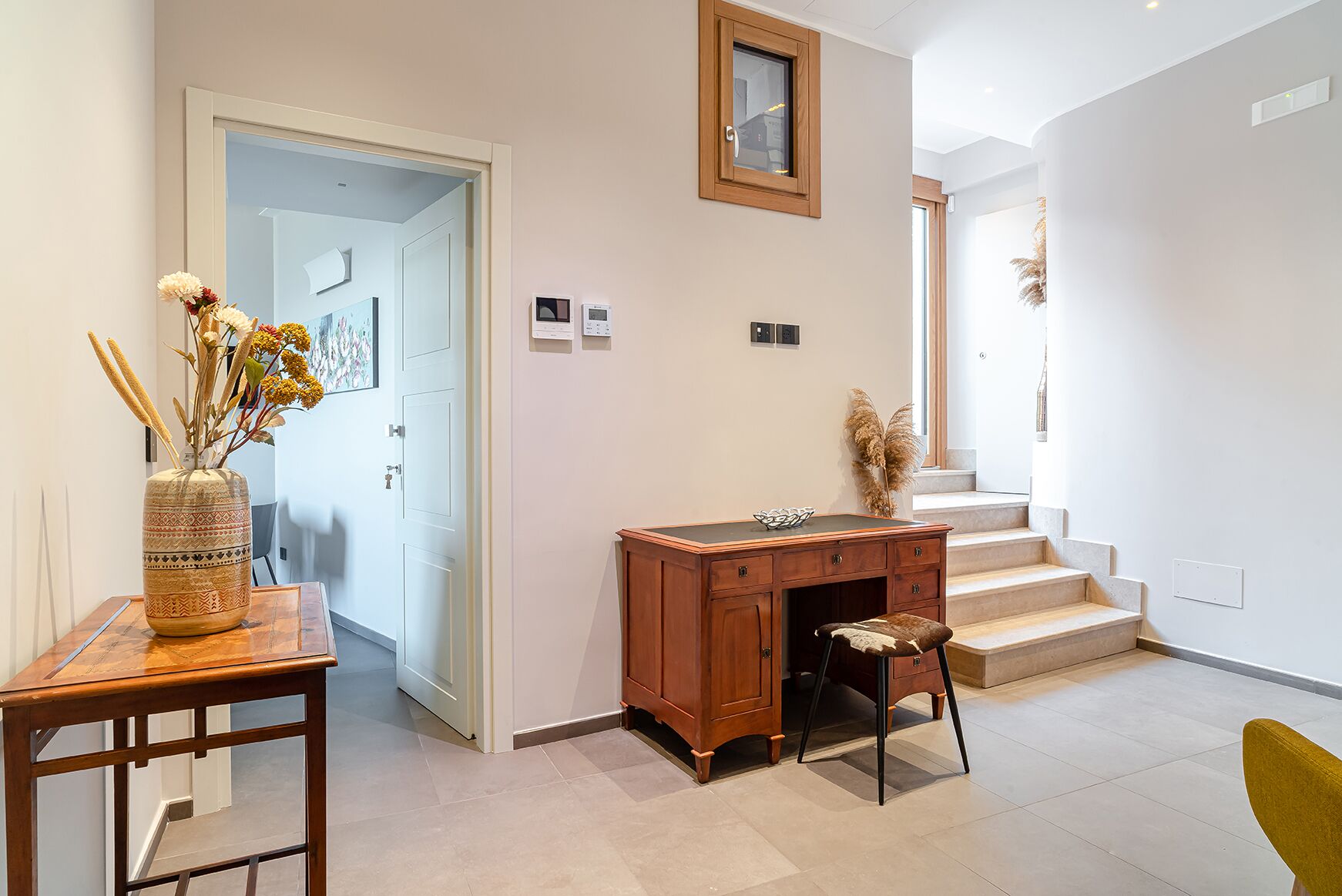 A hallway with a desk, chair, and a vase of dried flowers.