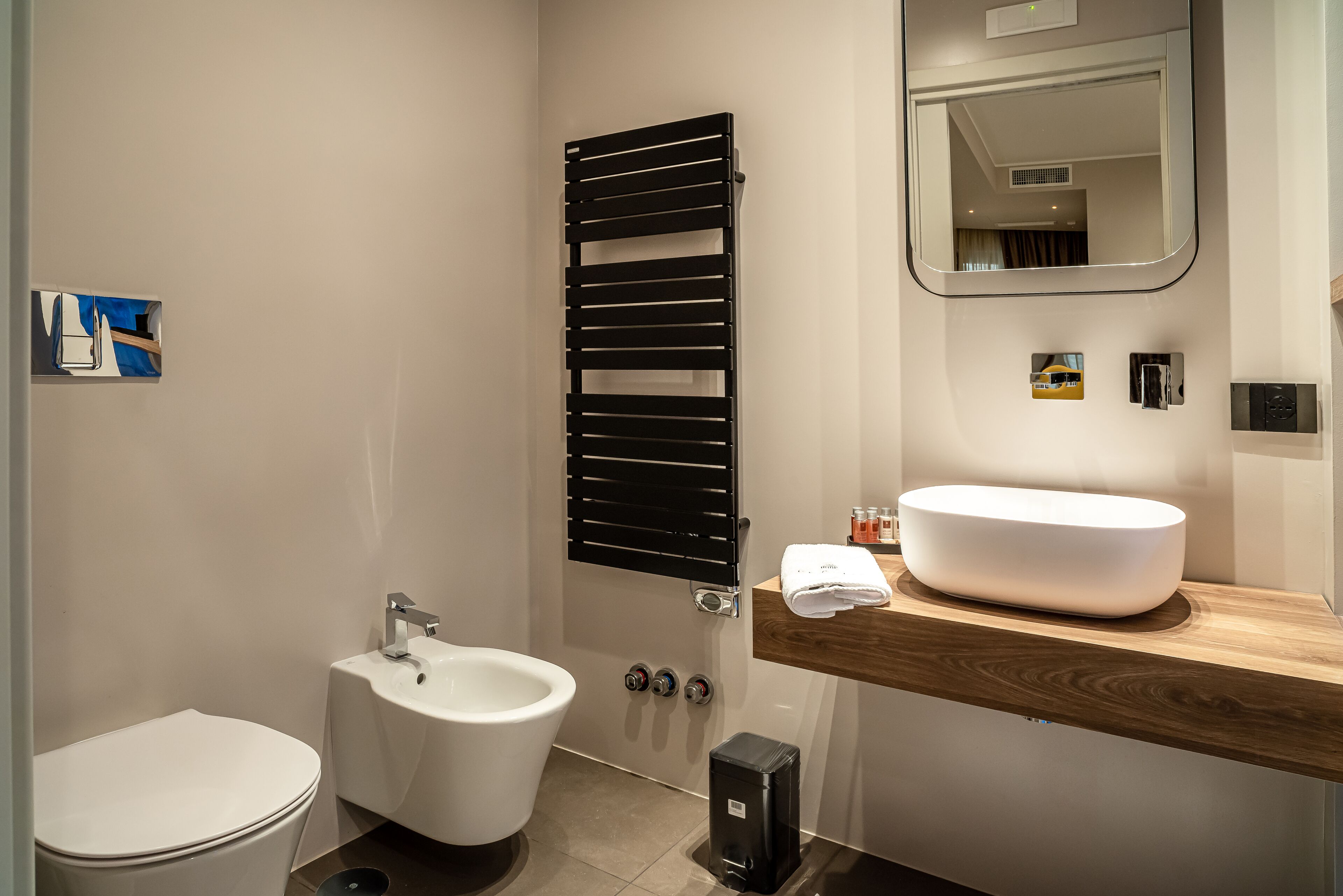 Ein modernes Badezimmer mit Toilette, Bidet und einem großen Spiegel über einem Holzwaschtisch mit Waschbecken.