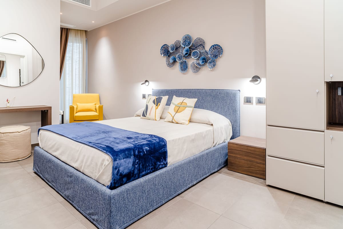 A modern bedroom with a large bed, a yellow armchair, a wall art piece, and a built-in wardrobe.