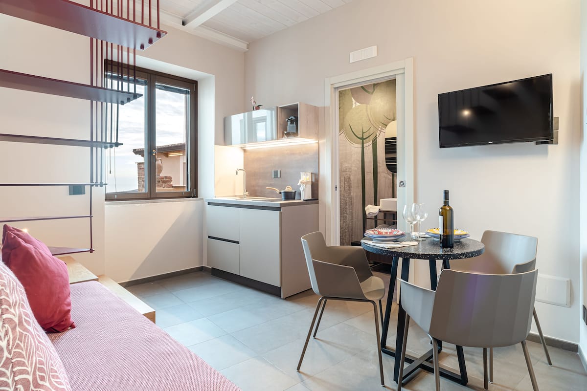 A modern kitchen with a dining area, a TV mounted on the wall, and a staircase leading to an upper level.