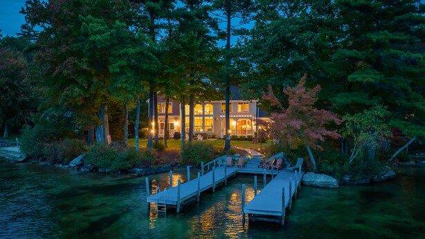 Une propriété au bord du lac, dotée d’un quai, d’une maison avec de nombreuses fenêtres et entourée d’arbres.