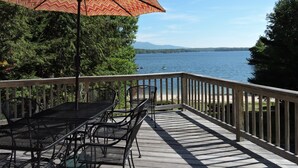 A wooden deck with a table and chairs, an umbrella, and a view of a lake with boats.