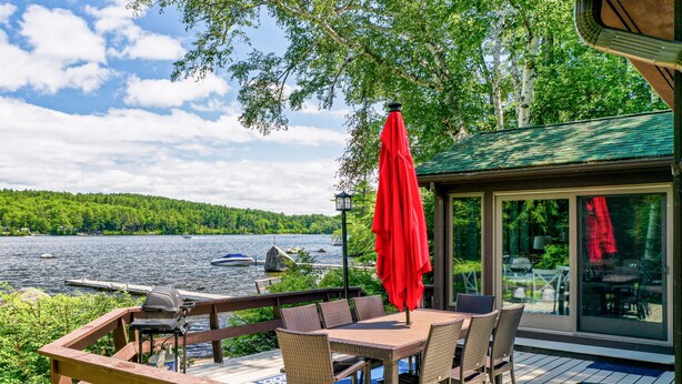 A deck with a table and chairs, overlooking a lake with boats.