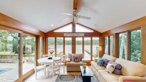 A spacious living room with a high ceiling, large windows, a ceiling fan, and a view of the lake.