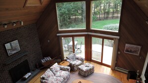A cozy living room with a fireplace, floral sofas, a coffee table, and a large window offering a view of the outdoors.