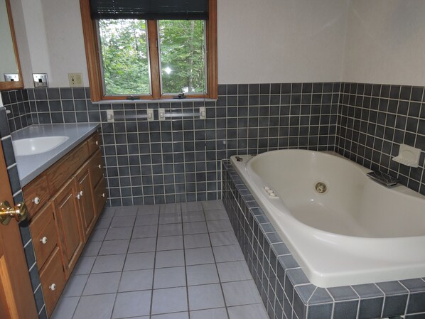 Une salle de bain avec une baignoire, un lavabo et une fenêtre donnant sur les arbres.