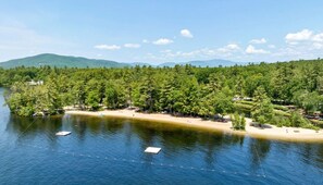 A lakeside property with a sandy beach, dense forest, and a boat dock. - Large Suissevale Winnipesaukee Home 2 Minute Walk To Beach (Moultonborough)