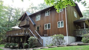 A two-story wooden house with a balcony, a covered porch, and a staircase leading to the upper level.