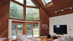 A spacious living room with a large sofa set, a flat-screen TV, and a wooden ceiling with skylights.