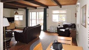 A spacious living room with a wooden ceiling, a black leather sofa, a wooden dining table, and a television. - Directly Across Street From Suissevale Winnipesaukee Beach (Moultonborough)