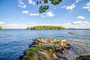 Une vue sur le lac, avec une rive rocheuse, un petit quai et une île boisée à l’horizon.