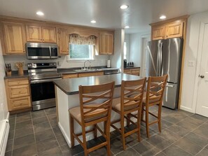 A kitchen with wooden cabinets, stainless steel appliances, a central island with chairs, and a large refrigerator.