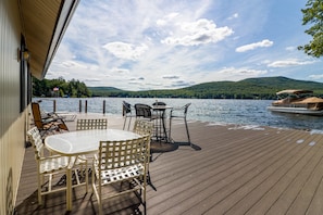 A wooden deck with outdoor seating, overlooking a lake and mountains.