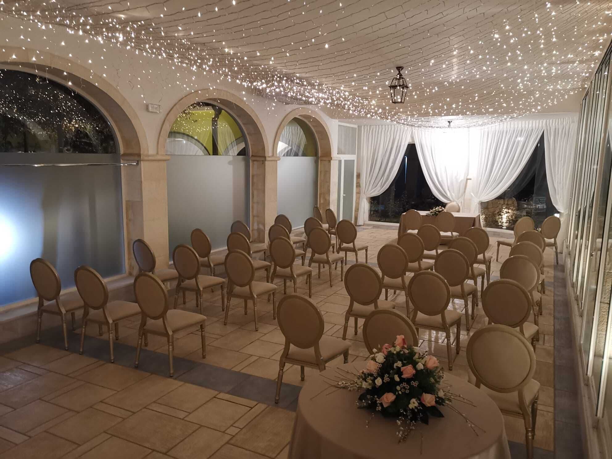 Um espaço interior com fileiras de cadeiras e mesas, portas em arco e um teto decorado com luzes.