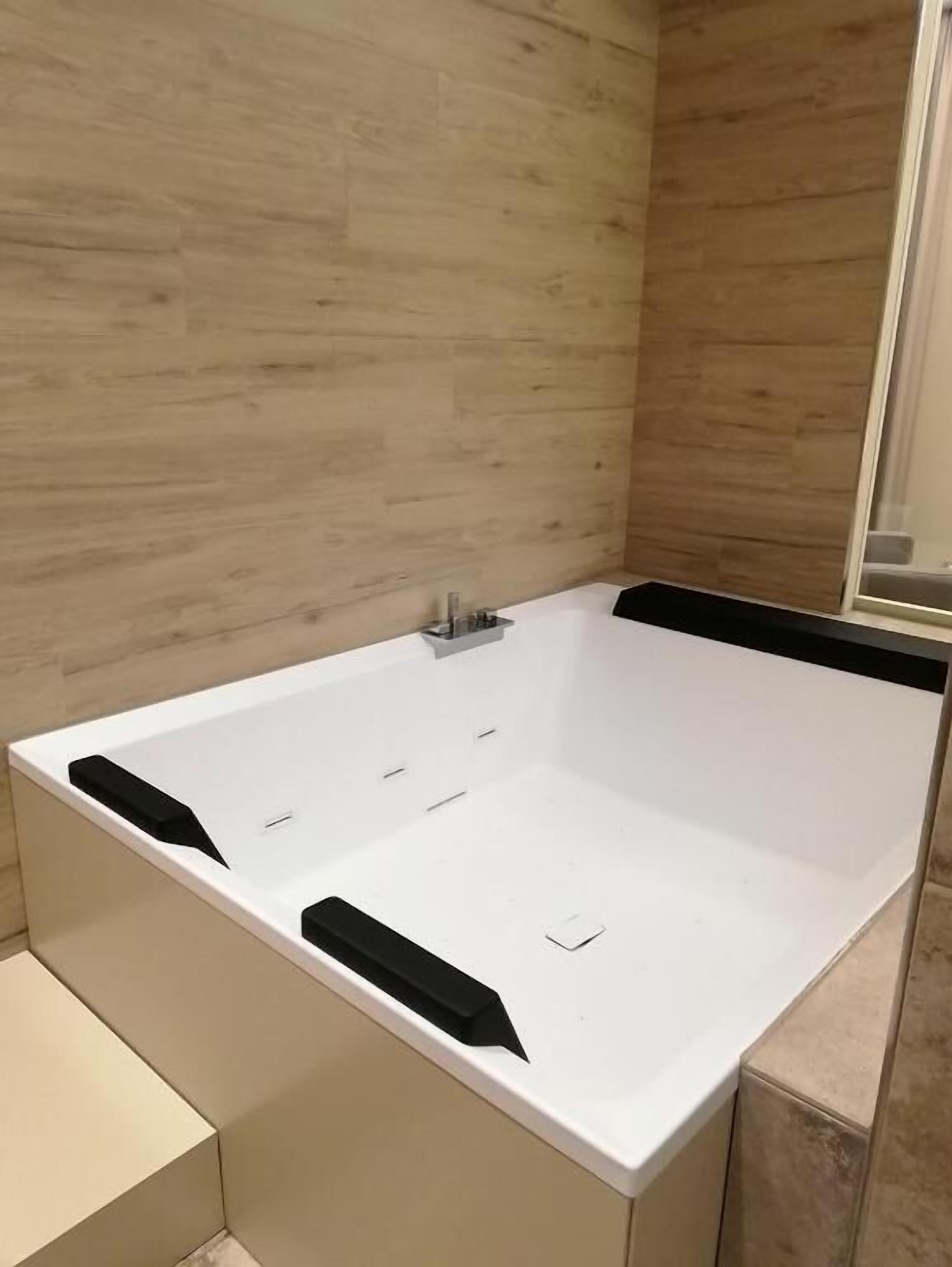A modern bathroom with a large bathtub, a shower area, and a wooden wall.