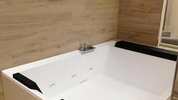 A modern bathroom with a large bathtub, a shower area, and a wooden wall.