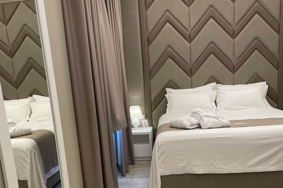 Habitación de hotel con una cama grande, una mesita de noche, un espejo y un cabecero con estampado en zigzag.