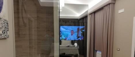 Una habitación de hotel moderna con una televisión de pantalla plana grande, un sofá y una cama con una mesita de noche.