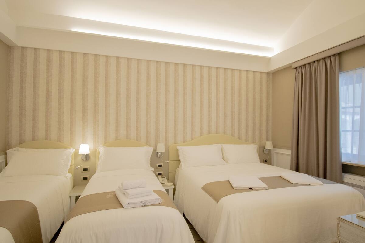 Habitación de hotel con dos camas, un ventanal con cortinas y una pared a rayas.
