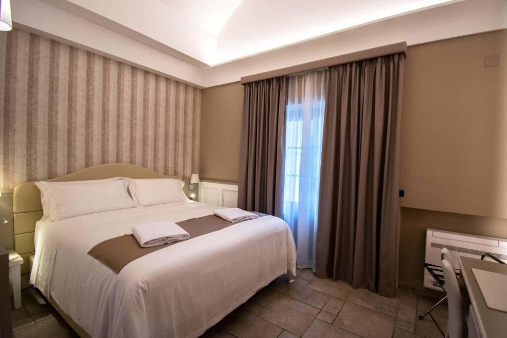 A hotel room with a large bed, a desk, and a window with curtains.